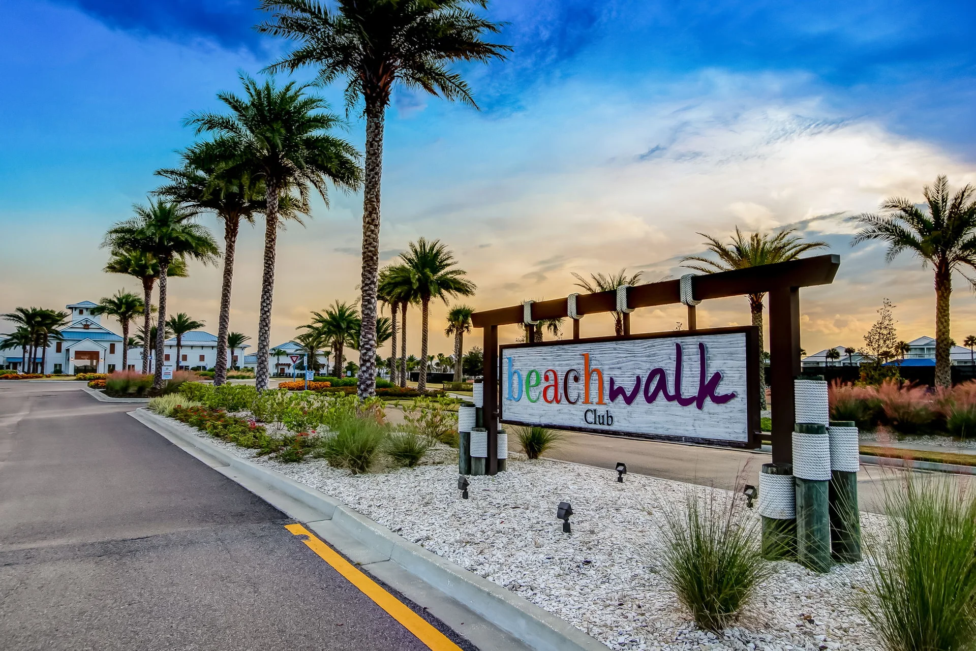 Beachwalk Club monument sign framed by palm trees at sunset